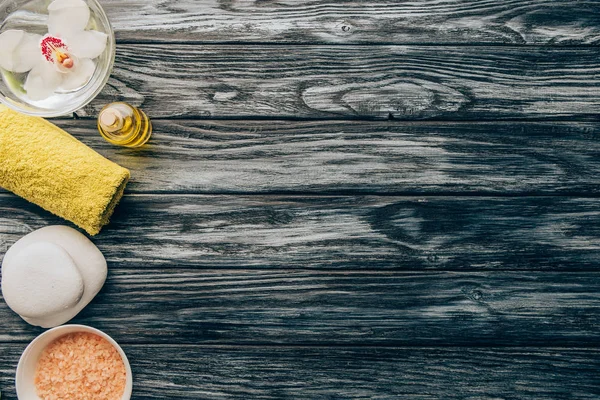 Vista dall'alto di asciugamano organizzato, olio essenziale, sale e orchidea fiore in ciotola per massaggi e spa su sfondo di legno — Foto stock