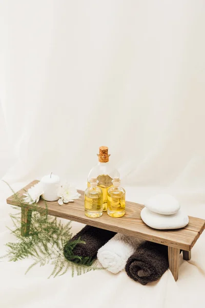 Close up view of arrangement of spa treatment accessories with fern plant, towels, oil and pebbles on white background — Stock Photo