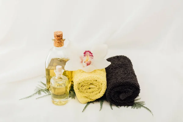 Vista de cerca de la disposición de los accesorios de tratamiento de spa con aceite, toallas y flor de orquídea sobre fondo blanco - foto de stock