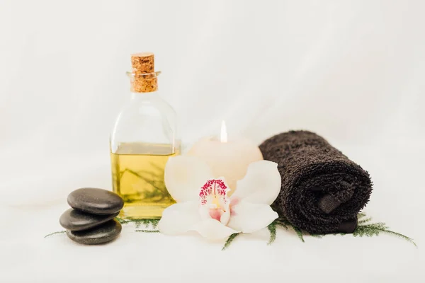 Close up view of arrangement of spa treatment accessories with oil, towel and orchid flower on white background — Stock Photo