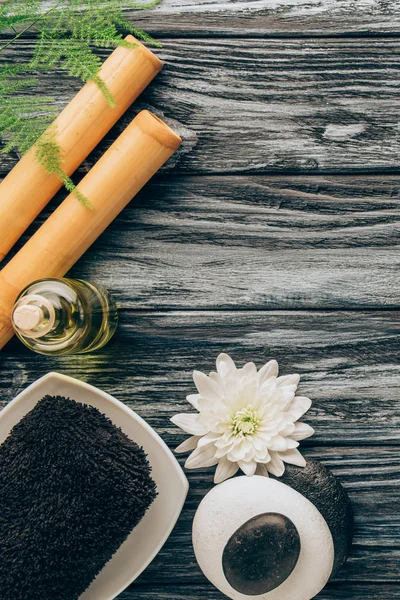 Flat lay with spa and massage treatment arrangement with towel, essential oil, pebbles and chrysanthemum flower on wooden tabletop — Stock Photo