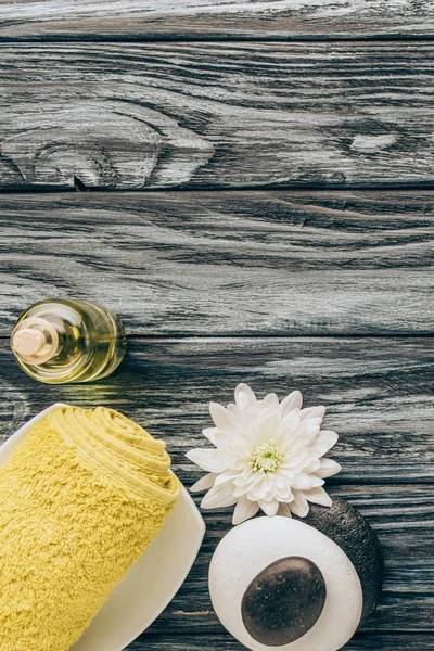 Flat lay with spa and massage treatment arrangement with towel, essential oil, pebbles and chrysanthemum flower on wooden background — Stock Photo