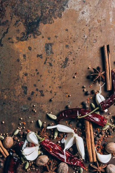 Top view of scattered chilli peppers, garlic and cinnamon sticks on grungy table — Stock Photo