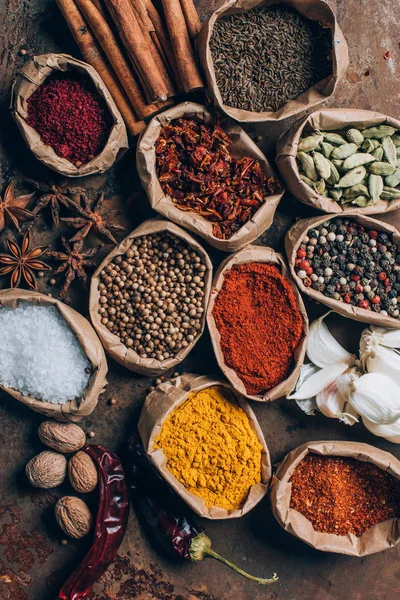 Vue du dessus du sel, des flocons de piment et du poivre en poudre dans des sacs en papier sur la table — Photo de stock