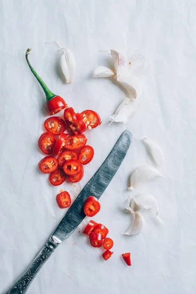 Vue du dessus du couteau et des morceaux de piment rouge sur la table blanche — Photo de stock