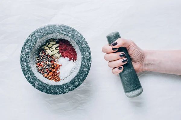 Cropped image of woman holding pestle near mortar with spices on white table — Stock Photo