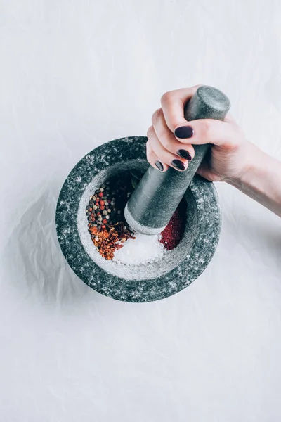 Cropped image of woman grinding spices in mortar on white table — Stock Photo