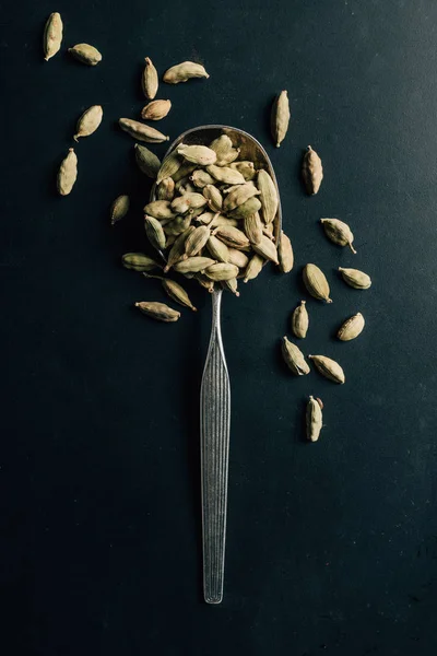Верхний вид семян кардамона на ложке и темном столе — стоковое фото