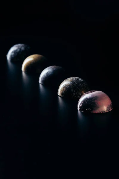 Doces de chocolate colocados em linha sobre fundo preto — Fotografia de Stock