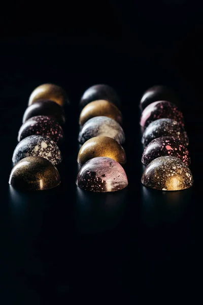 Différents bonbons au chocolat placés en rangées sur fond noir — Photo de stock