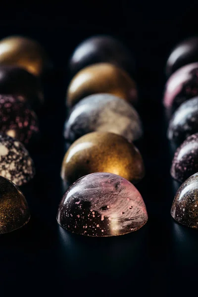 Vista de primer plano de diferentes caramelos de chocolate colocados en filas sobre fondo negro - foto de stock