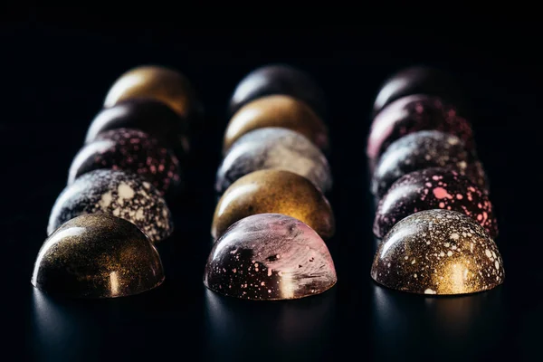 Imagen de primer plano de caramelos de chocolate colocados en filas sobre fondo negro - foto de stock