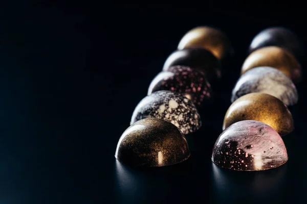 Varios caramelos de chocolate colocados en filas sobre fondo negro - foto de stock