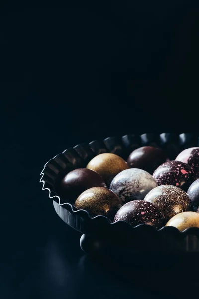 Closeup view of pile of different chocolate candies in bowl on black background — Stock Photo