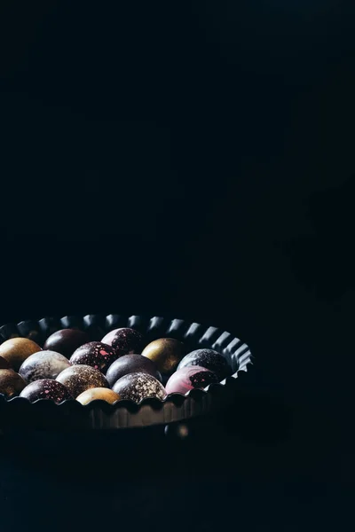Close up tiro de pilha de diferentes doces de chocolate em tigela no fundo preto — Stock Photo