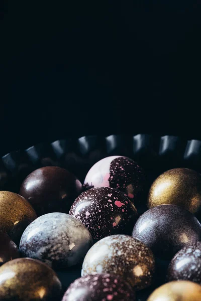 Closeup view of pile of different chocolate candies in bowl on black background — Stock Photo