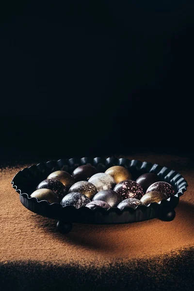 Haufen verschiedener Schokoladenbonbons in Schüssel auf der Oberfläche mit Kakaopulver — Stockfoto