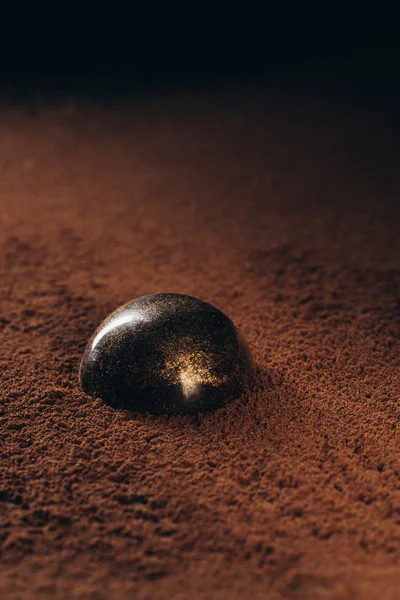 Closeup view of chocolate candy with golden splashes on surface with cocoa powder — Stock Photo