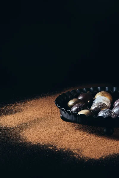 Close up view of pile of different chocolate candies in bowl on black background — Stock Photo