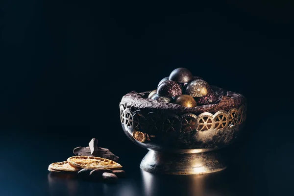 Closeup view of vintage bowl with candies, chocolate pieces, nuts and dry orange slices on black background — Stock Photo
