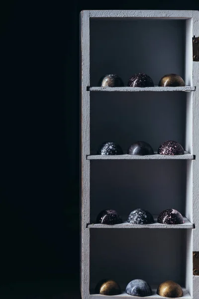 Різні шоколадні цукерки розміщені рядами на полицях на чорному тлі — стокове фото