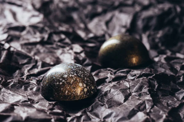 Крупный план двух шоколадных конфет с золотыми брызгами на скомканной бумаге — стоковое фото