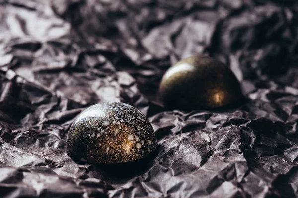 Primer plano de dos caramelos de chocolate con salpicaduras de oro sobre papel arrugado - foto de stock