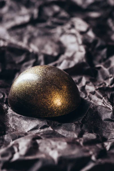 Closeup view of chocolate candy with golden splashes on crumpled paper — Stock Photo