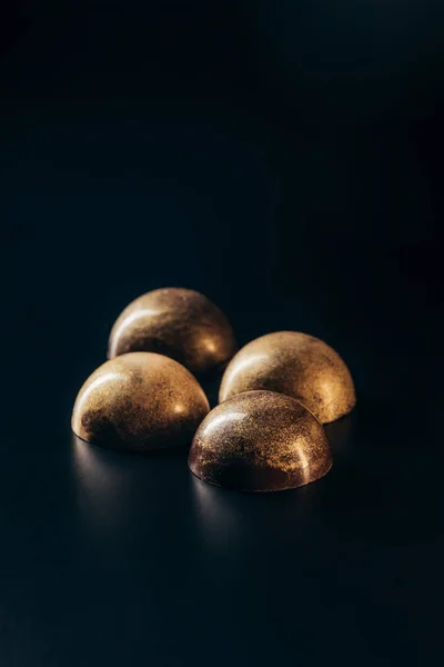 Closeup image of chocolate candies with golden splashes on black background — Stock Photo