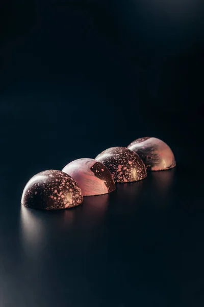 Chocolate candies with pink slpashes placed in row on black background — Stock Photo