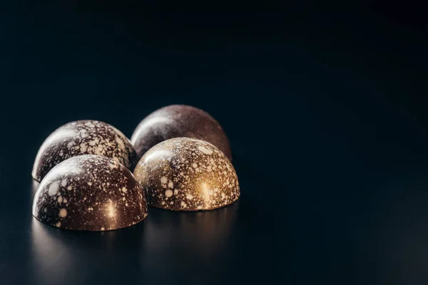 Imagen de primer plano de caramelos de chocolate con salpicaduras de oro sobre fondo negro - foto de stock