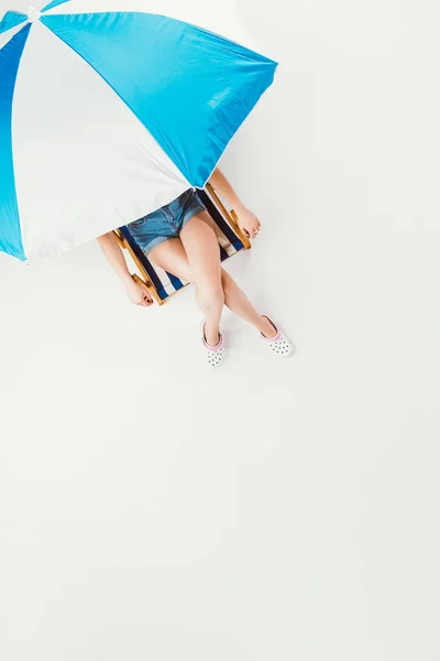 Vista superior da menina sentada na cadeira sob guarda-chuva praia isolado no branco — Fotografia de Stock