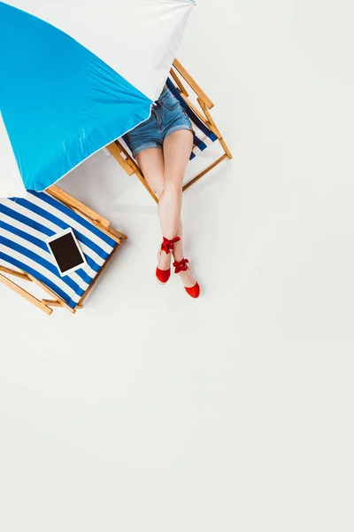 Вид сверху девушки, отдыхающей в кресле под пляжным зонтиком изолированный на белом — стоковое фото