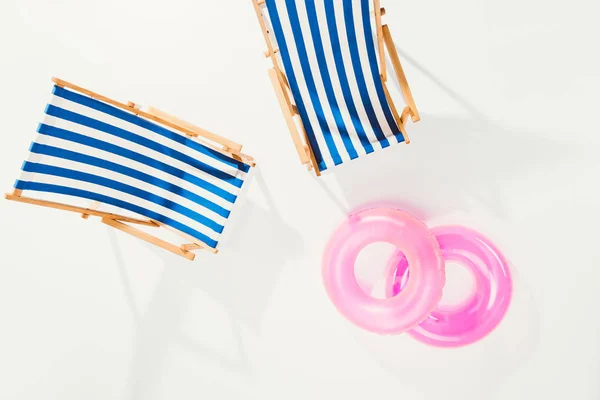 Vue de dessus des chaises de plage rayées et des anneaux gonflables isolés sur blanc — Photo de stock