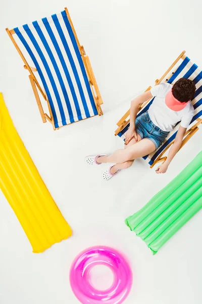 Vista aérea da menina descansando em cadeira de praia entre itens de praia isolados em branco — Fotografia de Stock