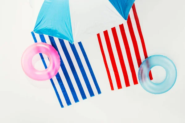 Top view of beach umbrella, striped towels and inflatable rings isolated on white — Stock Photo