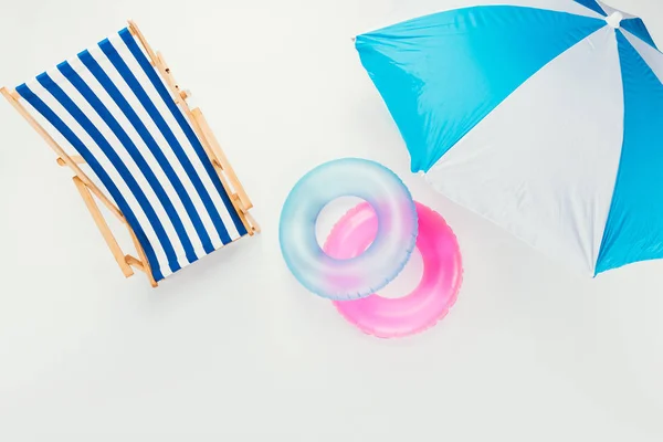 Vista superior de la sombrilla de playa, silla de playa a rayas y anillos inflables aislados en blanco - foto de stock