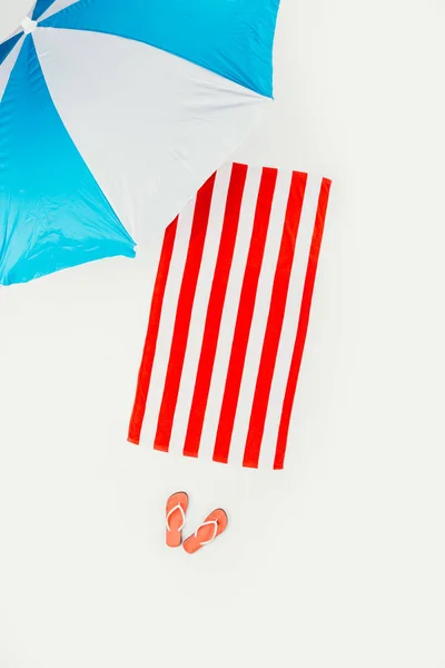 Vista superior de guarda-chuva de praia, toalha listrada e chinelos isolados em branco — Fotografia de Stock