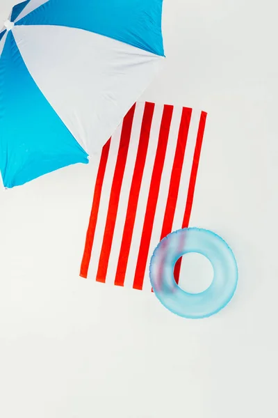 Vista superior de la sombrilla de playa, toalla rayada y anillo inflable aislado en blanco - foto de stock
