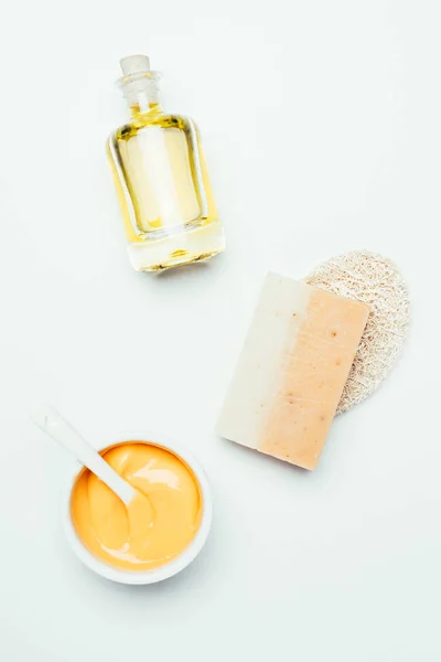 Flat lay with orange clay mask in container, spoon, sponge, soap and perfume bottle isolated on white surface — Stock Photo