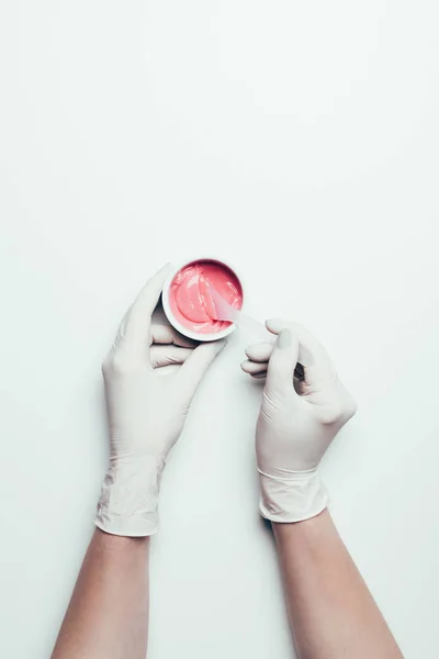 Schnappschuss einer Frau in Latex-Handschuhen, die mit einem Löffel auf weißer Oberfläche eine rosa Maske aus einem Behälter zieht — Stockfoto