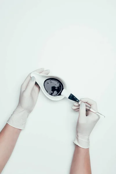 Cropped shot of woman in latex gloves holding black mask and brush isolated on white surface — Stock Photo