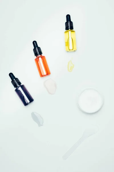 Pose plate avec des bouteilles cosmétiques avec tuyaux, taches, cuillère et masque d'argile dans un récipient isolé sur la surface blanche — Photo de stock