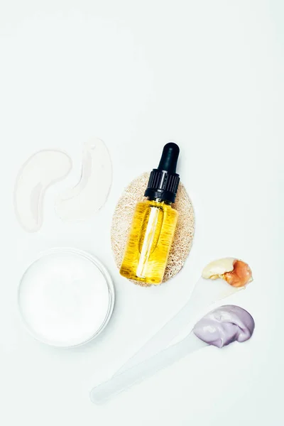 Pose plate avec des patchs pour les yeux, masque en argile dans le récipient, bouteille cosmétique, éponge et cuillères avec des masques en argile colorés isolés sur la surface blanche — Photo de stock