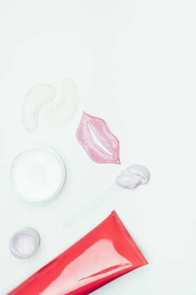 Vista dall'alto di maschera labbra, macchie oculari, maschera di argilla in contenitore e bottiglia di crema isolata su superficie bianca — Foto stock