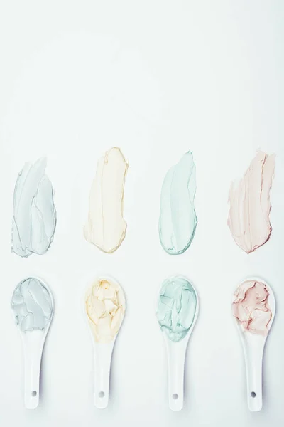 Top view of spoons and colorful clay mask smudges placed in row on white surface — Stock Photo