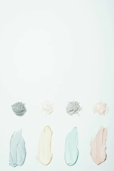 Flat lay with different clay powder and colorful clay mask smudges placed in row isolated on white surface — Stock Photo