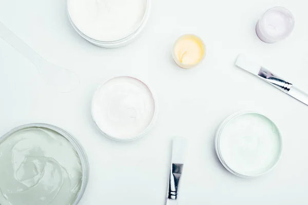 Flat lay with different clay masks in containers and brushes isolated on white surface — Stock Photo