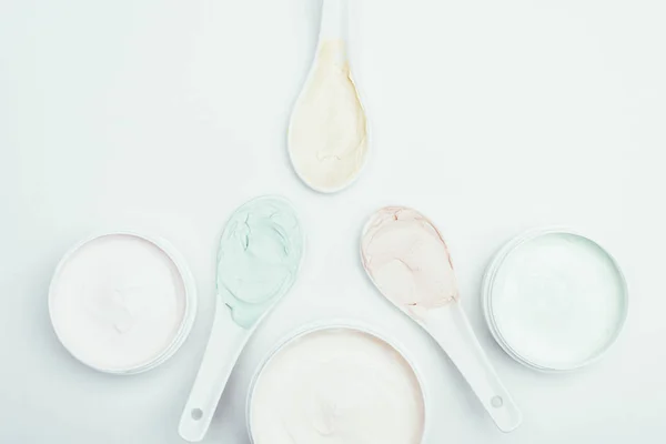 Flat lay with various colorful clay masks in containers and spoons isolated on white surface — Stock Photo