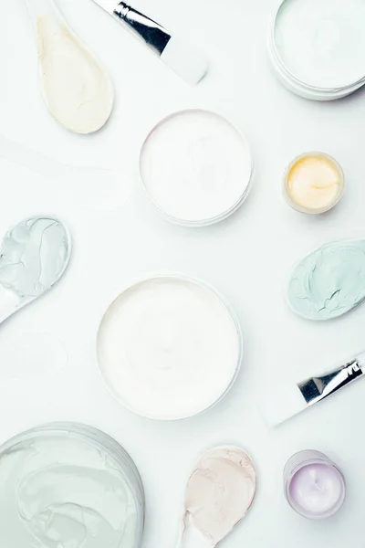 Flat lay with various clay masks in containers, spoons and brushes isolated on white surface — Stock Photo